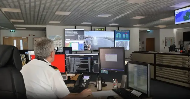 Maritime operations officer monitoring vessel activity and live camera feeds on multiple control-room screens